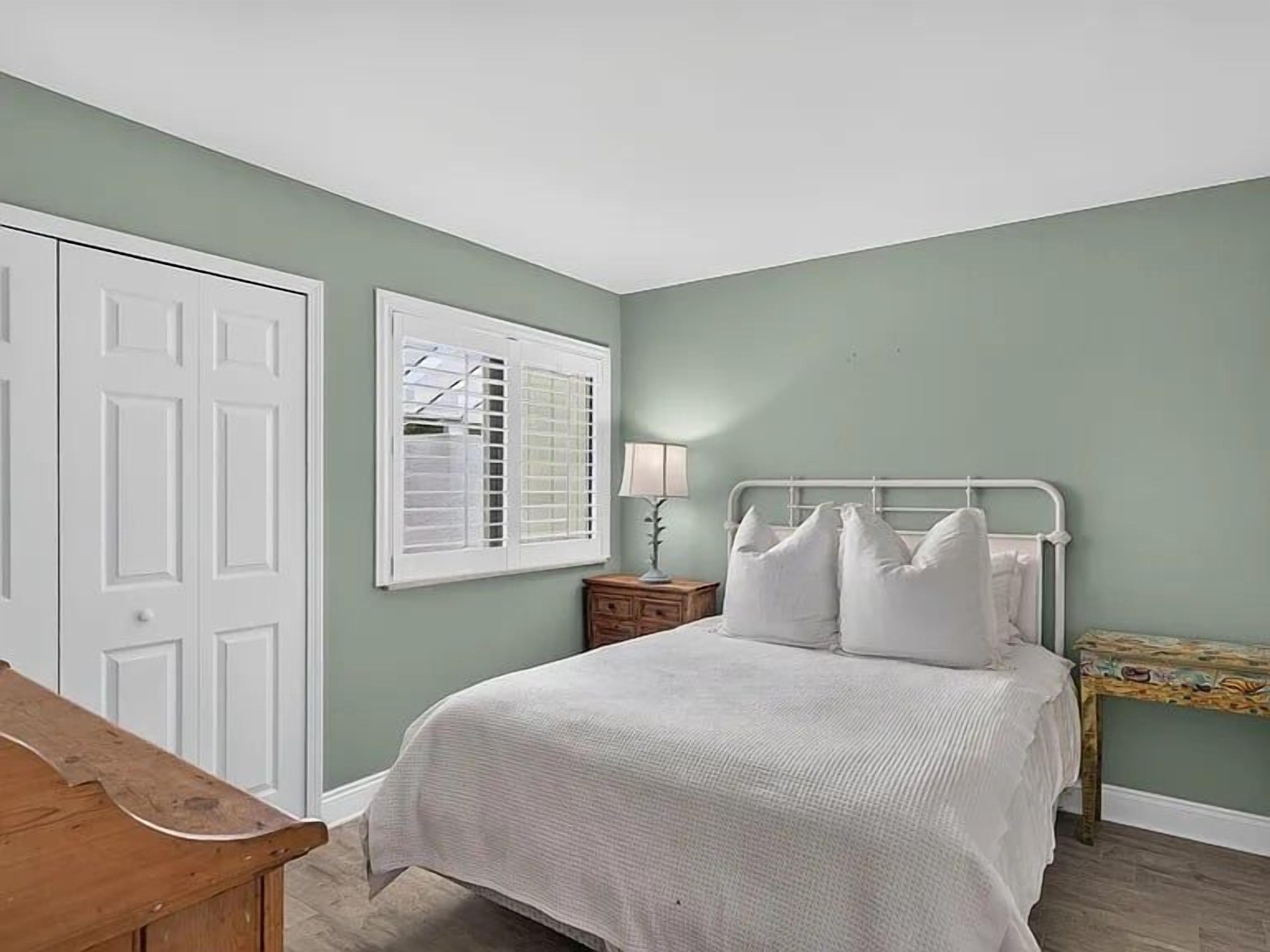 Un dormitorio con cama, mesita de noche, lámpara y ventana con persianas.