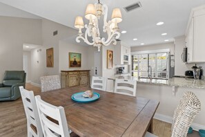 A dining area with a wooden table, white chairs, and a chandelier. - New! Sandestin Cottage w/ Golf Cart, Pool, Beach Access, Dog Friendly & Fenced Yard (Miramar Beach)