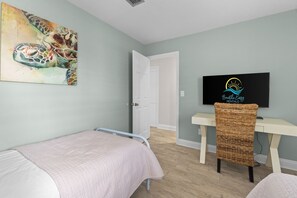 A bedroom with a bed, a desk, a chair, a television, and a painting on the wall. - New! Sandestin Cottage w/ Golf Cart, Pool, Beach Access, Dog Friendly & Fenced Yard (Miramar Beach)