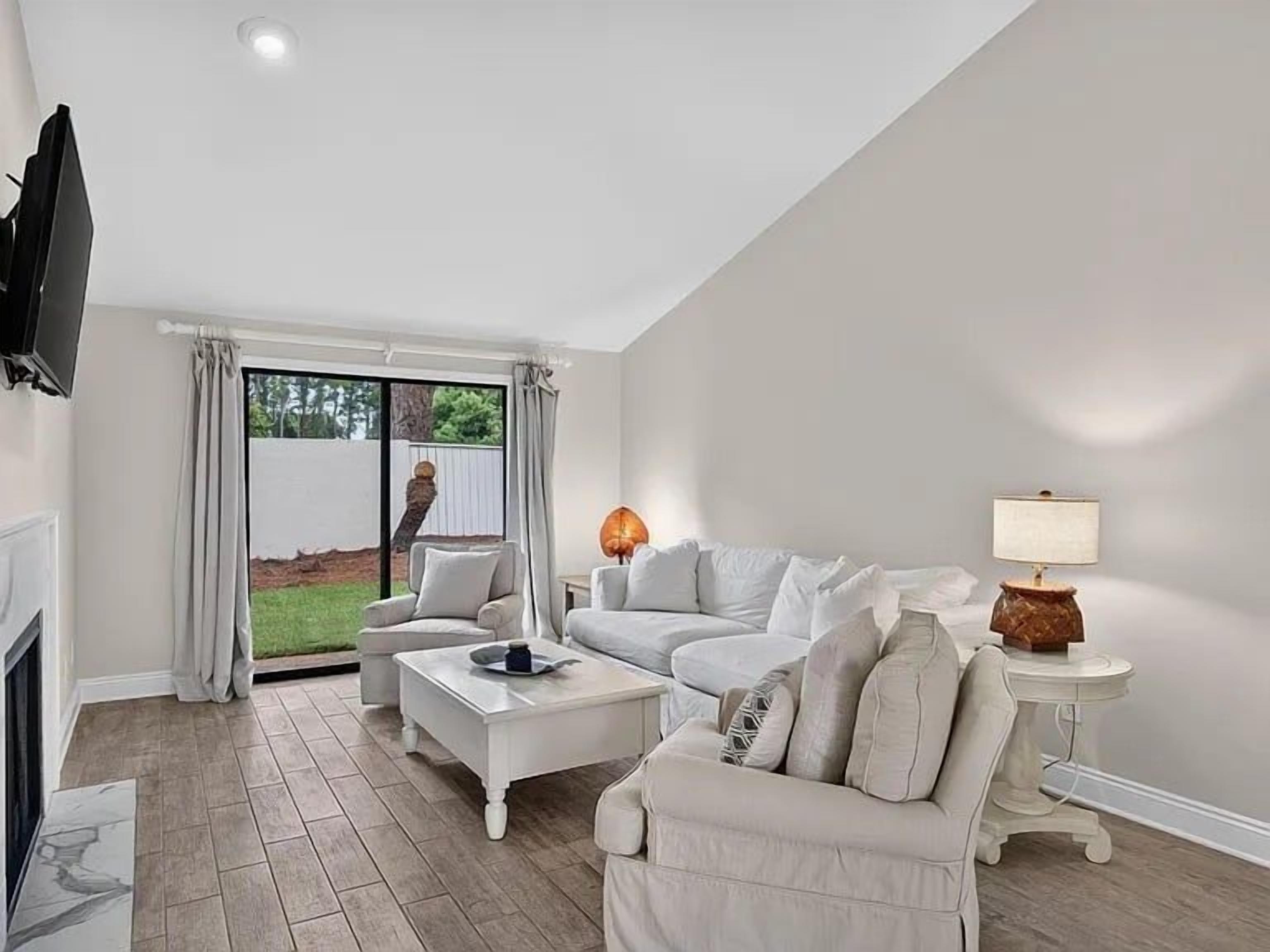 A modern living room with a fireplace, a television mounted on the wall, and a large sliding glass door leading to a garden.
