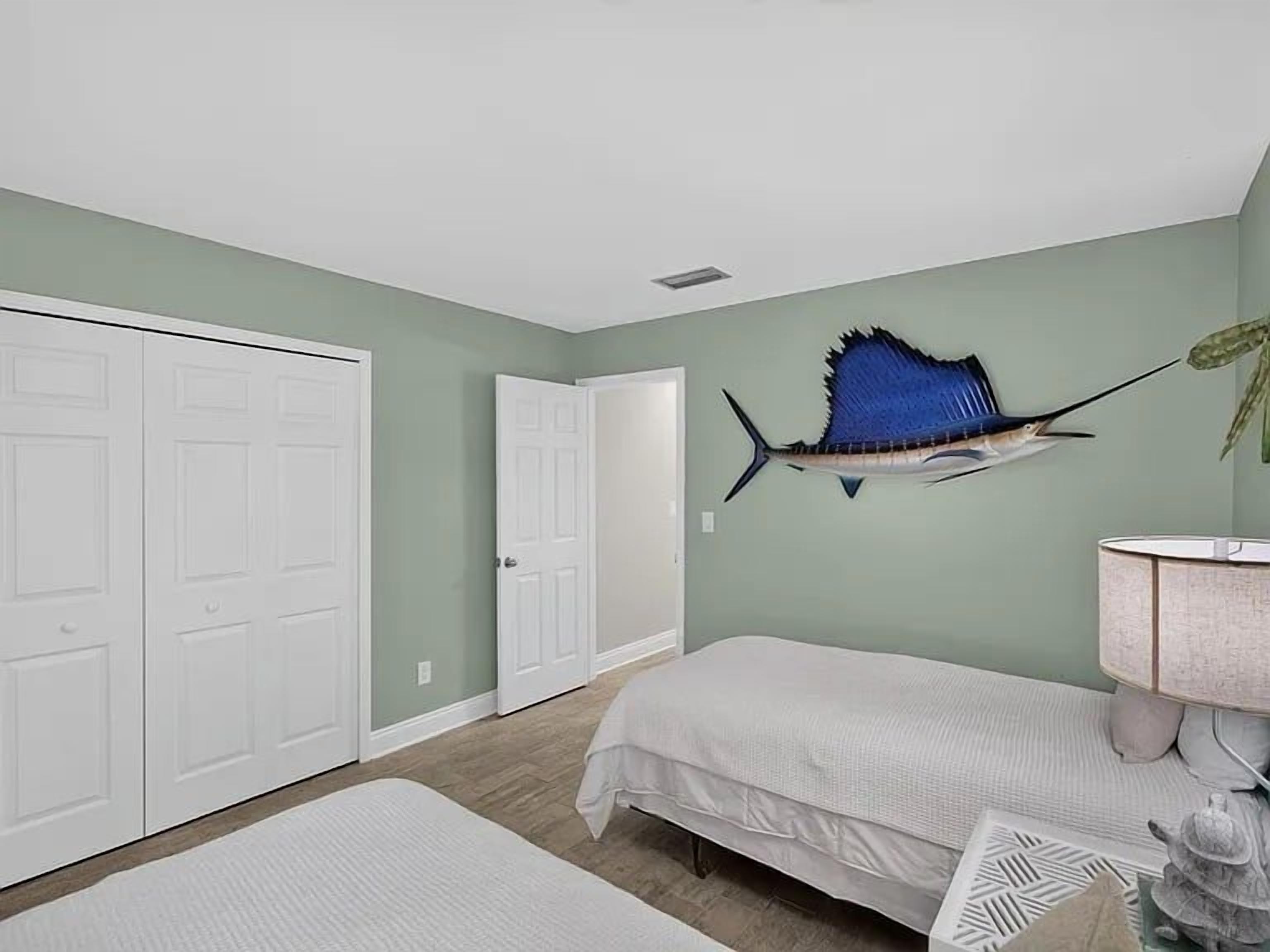 A bedroom with a bed, a white wardrobe, a door, and a wall-mounted fish decoration.