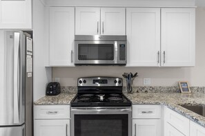 A kitchen with white cabinets, a stainless steel microwave, a stove, and a refrigerator. - New! Sandestin Cottage w/ Golf Cart, Pool, Beach Access, Dog Friendly & Fenced Yard (Miramar Beach)
