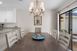 A dining area with a wooden table, white chairs, a chandelier, and a framed picture on the wall. - New! Sandestin Cottage w/ Golf Cart, Pool, Beach Access, Dog Friendly & Fenced Yard (Miramar Beach)