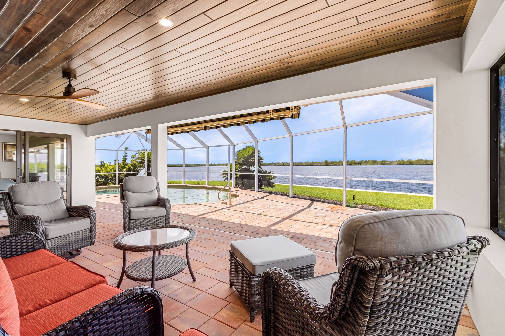 A covered patio area with wicker furniture, a glass table, and a view of a lake.