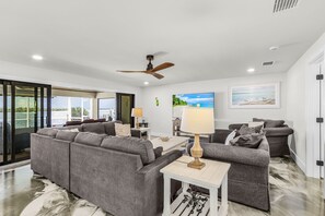 A spacious living area with a large gray sectional sofa, a smaller gray sofa, a wooden coffee table, and a ceiling fan. - Coastal Elegance with Breathtaking Matlacha Pass Views (Matlacha)