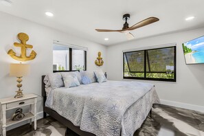 A bedroom with a bed, a nightstand, a ceiling fan, and a window with blinds. - Coastal Elegance with Breathtaking Matlacha Pass Views (Matlacha)