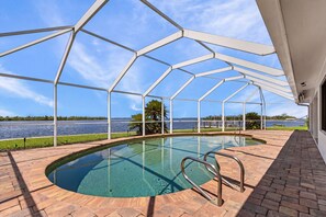 A swimming pool with a metal roof structure, surrounded by a brick patio, and overlooking a body of water. - Coastal Elegance with Breathtaking Matlacha Pass Views (Matlacha)