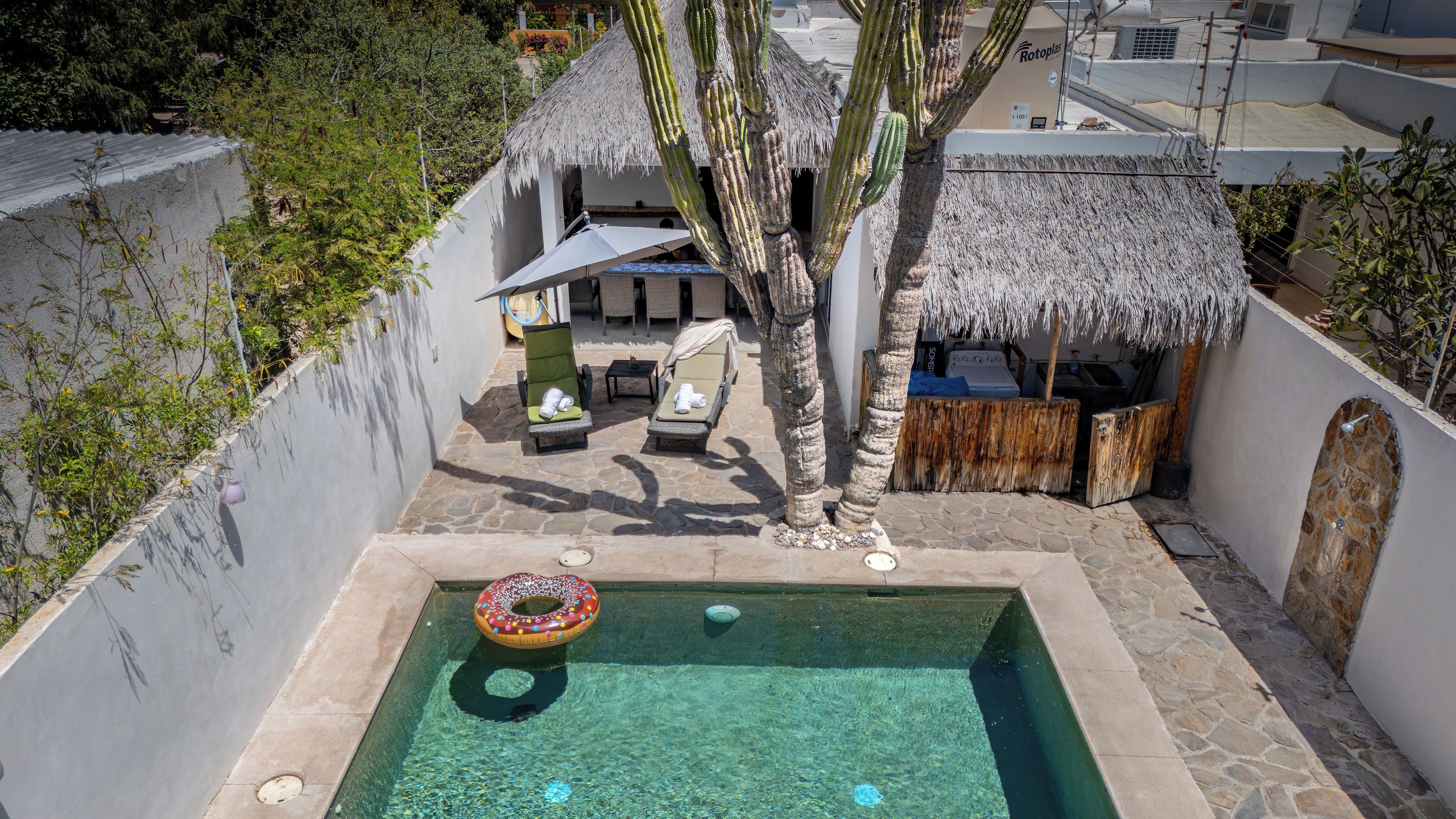Una piscina con un flotador con forma de dona, una estructura con techo de paja y un muro de piedra.