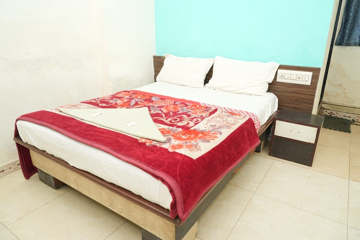 Uma cama com colcha vermelha e branca, cabeceira de madeira e uma mesinha de cabeceira com tomada.