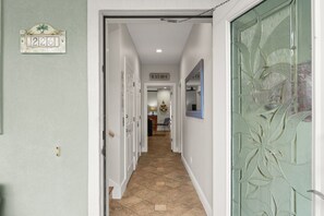 Een gang met een deur waarop 'BEACH HOUSE' staat, leidend naar een kamer met een decor in strandthema.