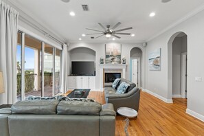 A spacious living room with a grey sofa, a television, and a fireplace. - ☀️ Seas the Day | Ocean Views | Steps 2 Beach | Private Pool | Free Golf (Miramar Beach)