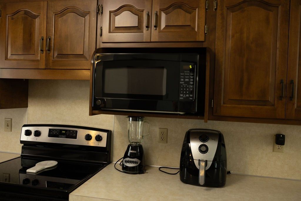 A kitchen with wooden cabinets, a microwave, a stove, a blender, and a toaster.