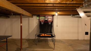 Ein Kellerraum mit einem Basketballkorb, einem Metallregal mit Sportbällen und einem Tischtennis-Tisch.