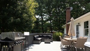 Eine Terrasse im Freien mit Grill, Sitzgelegenheit und Tisch mit Stühlen.