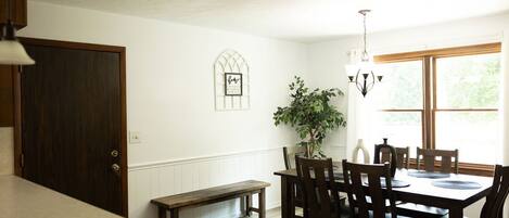 A dining area with a wooden table and chairs, a bench, a potted plant, and a window with natural light.