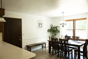 Un comedor con mesa y sillas de madera, una banca, una planta en maceta y una ventana con luz natural.
