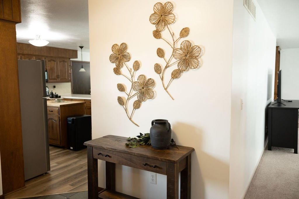 A kitchen with wooden cabinets, a refrigerator, a coffee machine, and a decorative wall piece.