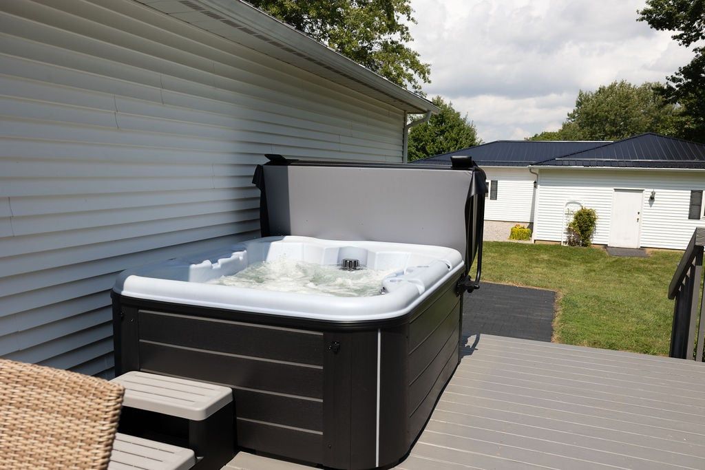 A hot tub on an outdoor deck with steps leading up to it, surrounded by a residential area.