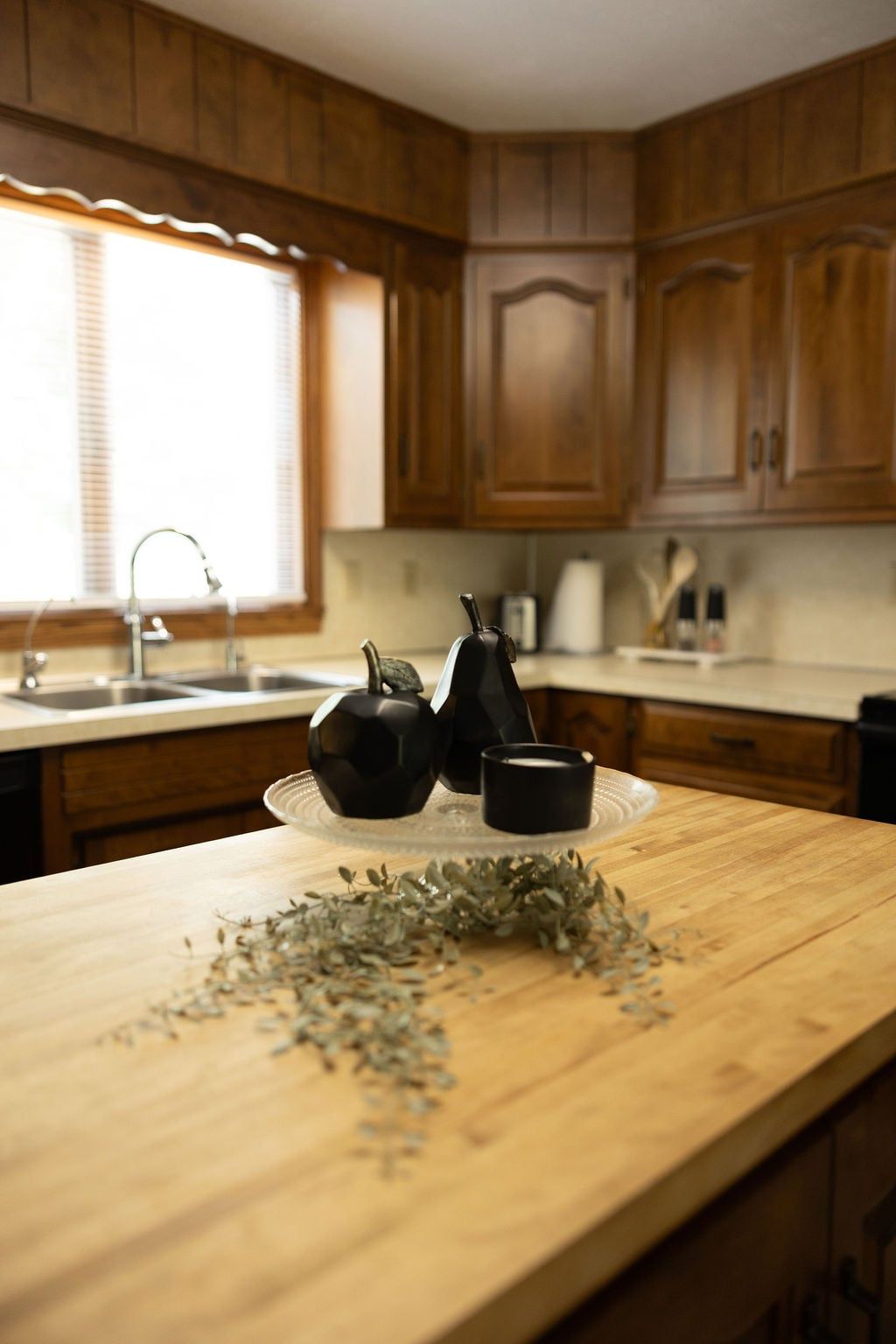A kitchen with wooden cabinets, a sink, and a countertop with a tea set and herbs.