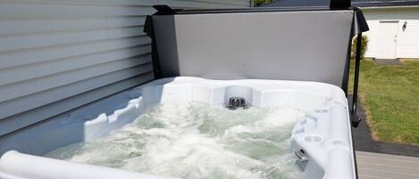 Un bain à remous à l’extérieur, de couleur blanche, placé à côté d’une maison dont le revêtement extérieur est également blanc et dont le toit est foncé.