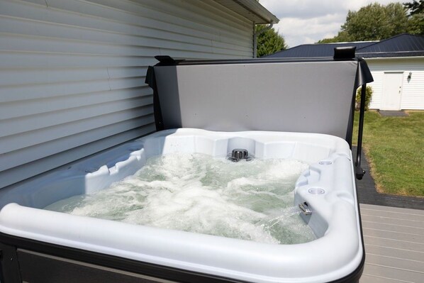 Un jacuzzi con revestimiento blanco, ubicado al aire libre junto a una casa de fachada blanca y techo oscuro.