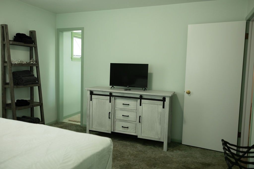 A bedroom with a bed, a white dresser with drawers, a television on top, and a wooden ladder against the wall.