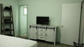 A bedroom with a bed, a white dresser with drawers, a television on top, and a wooden ladder against the wall.