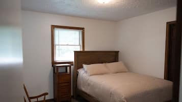 Ein Schlafzimmer mit einem hölzernen Bett, einem Nachttisch, einem Stuhl und einem Fenster.
