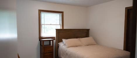 Un dormitorio con una cama de madera, una mesita de noche, una silla y un ventanal.