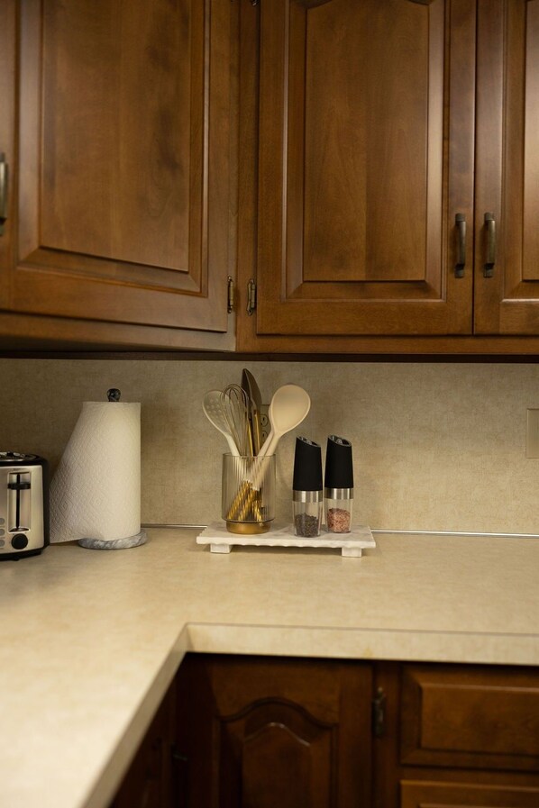 A kitchen with wooden cabinets, a countertop, a paper towel holder, a spice rack, and a toaster.