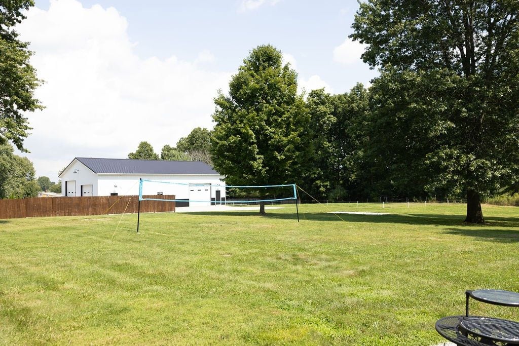 Ein grüner Hinterhof mit Volleyballnetz, einem weißen Gebäude und einem Baum.