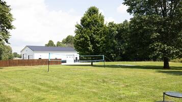 Ein grüner Hinterhof mit Volleyballnetz, einem weißen Gebäude und einem Baum.
