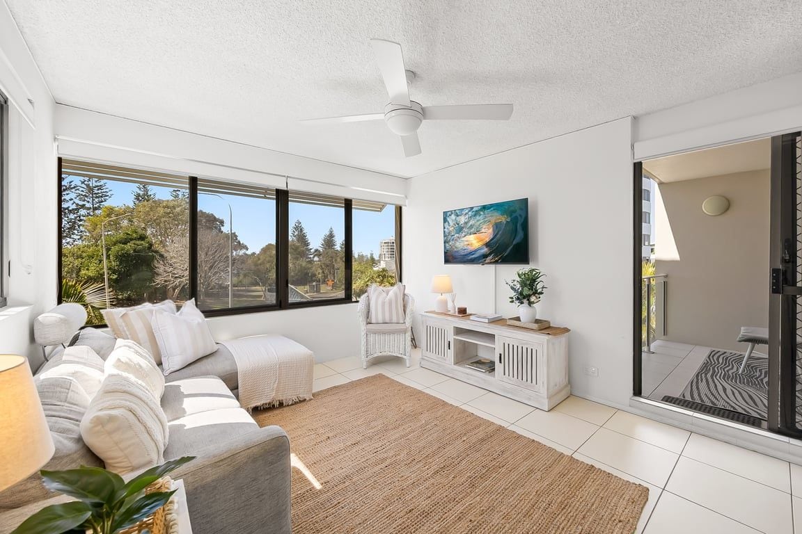 Un salon moderne avec un canapé, un tapis, une table d’appoint, un tableau et une grande fenêtre.