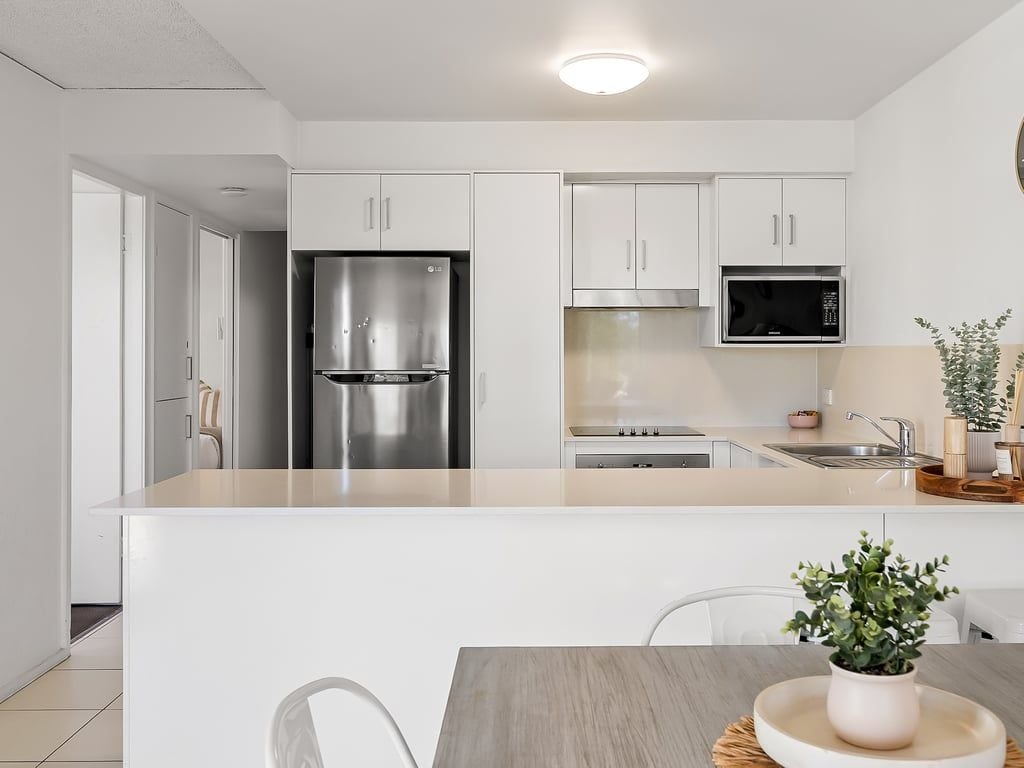 A modern kitchen with white cabinets, a stainless steel refrigerator, a microwave, and a sink.