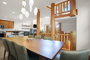 Ein geräumiger Essbereich mit Holztisch und -stühlen, im Hintergrund eine Küche und eine Treppe, die in eine obere Etage führt.