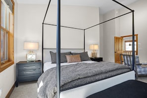 A four-poster canopy bed with a grey and white bedspread, two bedside tables with lamps, a wooden door, and a window with blinds. - New Listing - Custom Furnishings - Ski Season Shuttle - Community Pool & Hot Tub (Steamboat Springs)