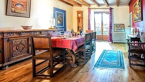 A dining area with a wooden table, chairs, and a red tablecloth. There is a clock on the wall and a window with curtains. - 2 vacation rentals in Burgundy for 11 people Nature, optional spa, and pets welcome! (Recey-sur-Ource)