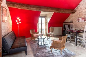Una habitación con techo rojo, un sofá de cuero negro, sillas de mimbre, una mesita redonda y una mesa de comedor con sillas.