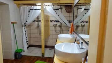 A bathroom with two sinks, a shower, and a mop leaning against the wall.