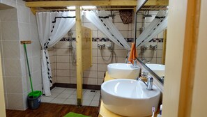 Un baño con dos lavamanos, una ducha y un trapeador apoyado en la pared.