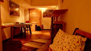 Una habitación acogedora con una mesa de madera, sillas, un tapete estampado y una cama con un cojín floral.