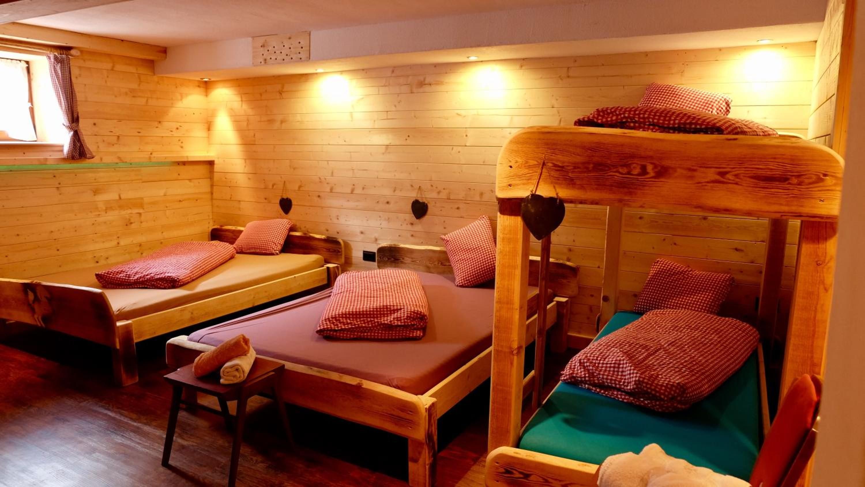 A cabin with wooden walls and floors, two single beds with red checkered bedding, a bench, and a small table with a towel.
