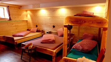 A cabin with wooden walls and floors, two single beds with red checkered bedding, a bench, and a small table with a towel.