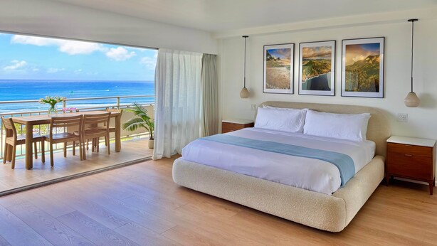 A bedroom with a large bed, a balcony with a view of the ocean, and three framed pictures on the wall. - NEWLY Remodeled - Oceanfront Paradise (Honolulu)