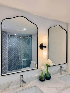 A bathroom with a large mirror, two sinks, and a shower with a herringbone tile pattern. - NEWLY Remodeled - Oceanfront Paradise (Honolulu)