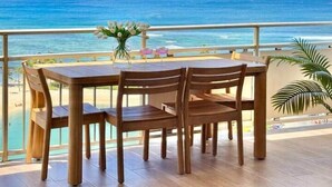 A balcony with a wooden table and chairs, overlooking a beach and ocean. - NEWLY Remodeled - Oceanfront Paradise (Honolulu)