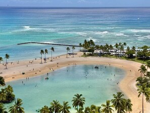 A beach with clear turquoise water, palm trees, and a pier extending into the sea. - NEWLY Remodeled Oceanfront Fireworks Every Friday (Honolulu)