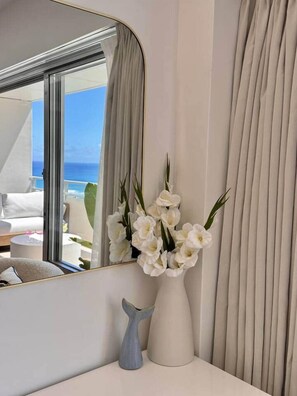 A room with a large mirror reflecting a balcony, a vase with white flowers, and a white vase on a table. - NEWLY Remodeled Oceanfront Fireworks Every Friday (Honolulu)