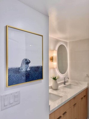 A modern bathroom with a large mirror, a sink, and a framed artwork of a seal. - NEWLY Remodeled Oceanfront Fireworks Every Friday (Honolulu)