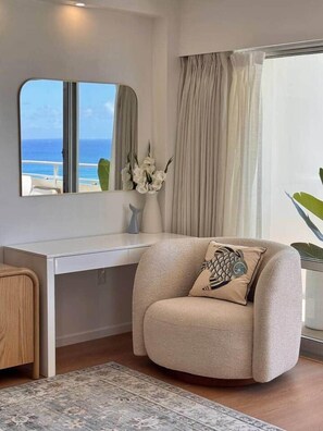 A modern room with a white desk, a beige armchair, a large mirror, and a view of the ocean. - NEWLY Remodeled Oceanfront Fireworks Every Friday (Honolulu)